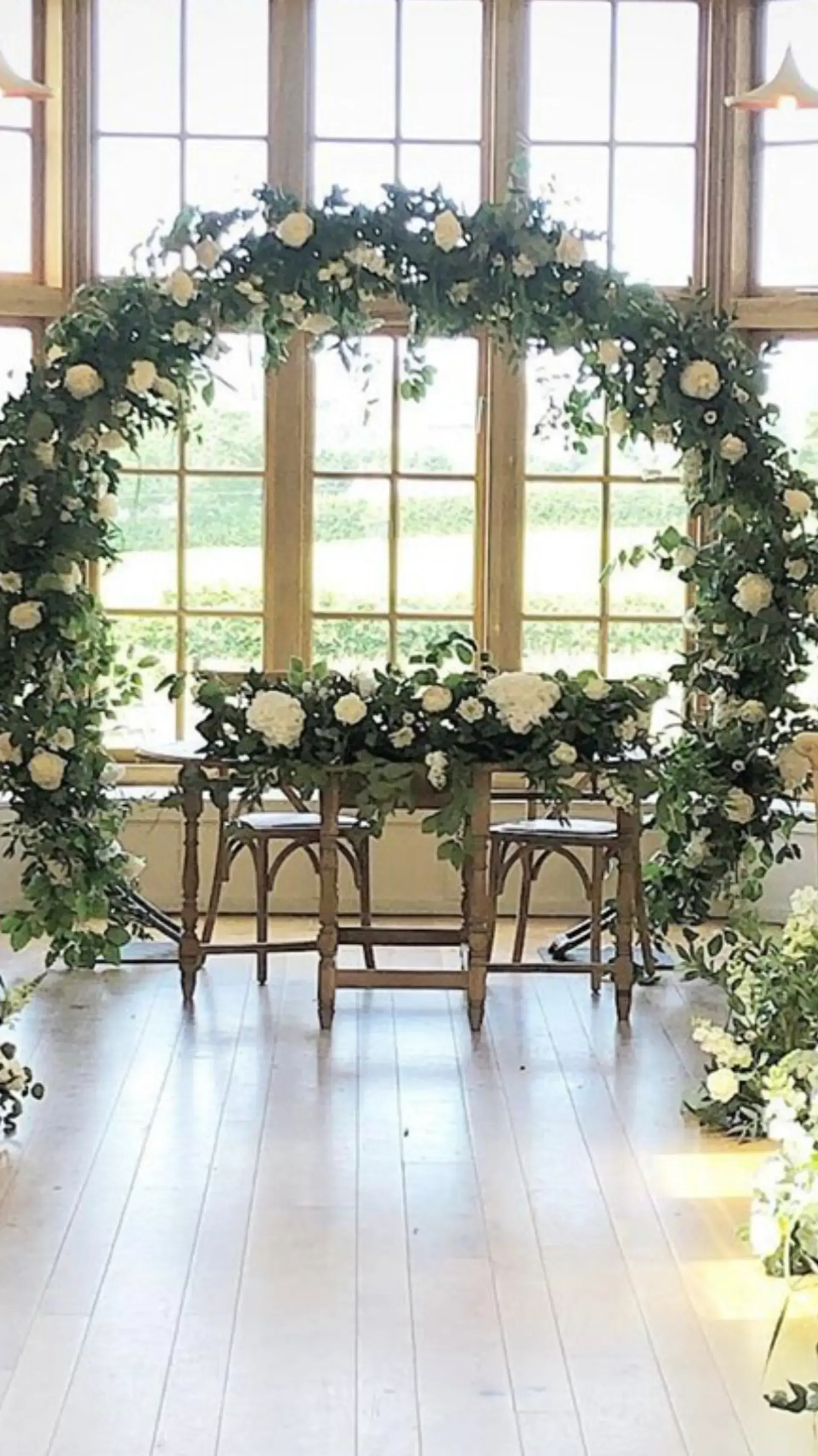 Floral arch over a white table and chairs in a bright room with tall windows