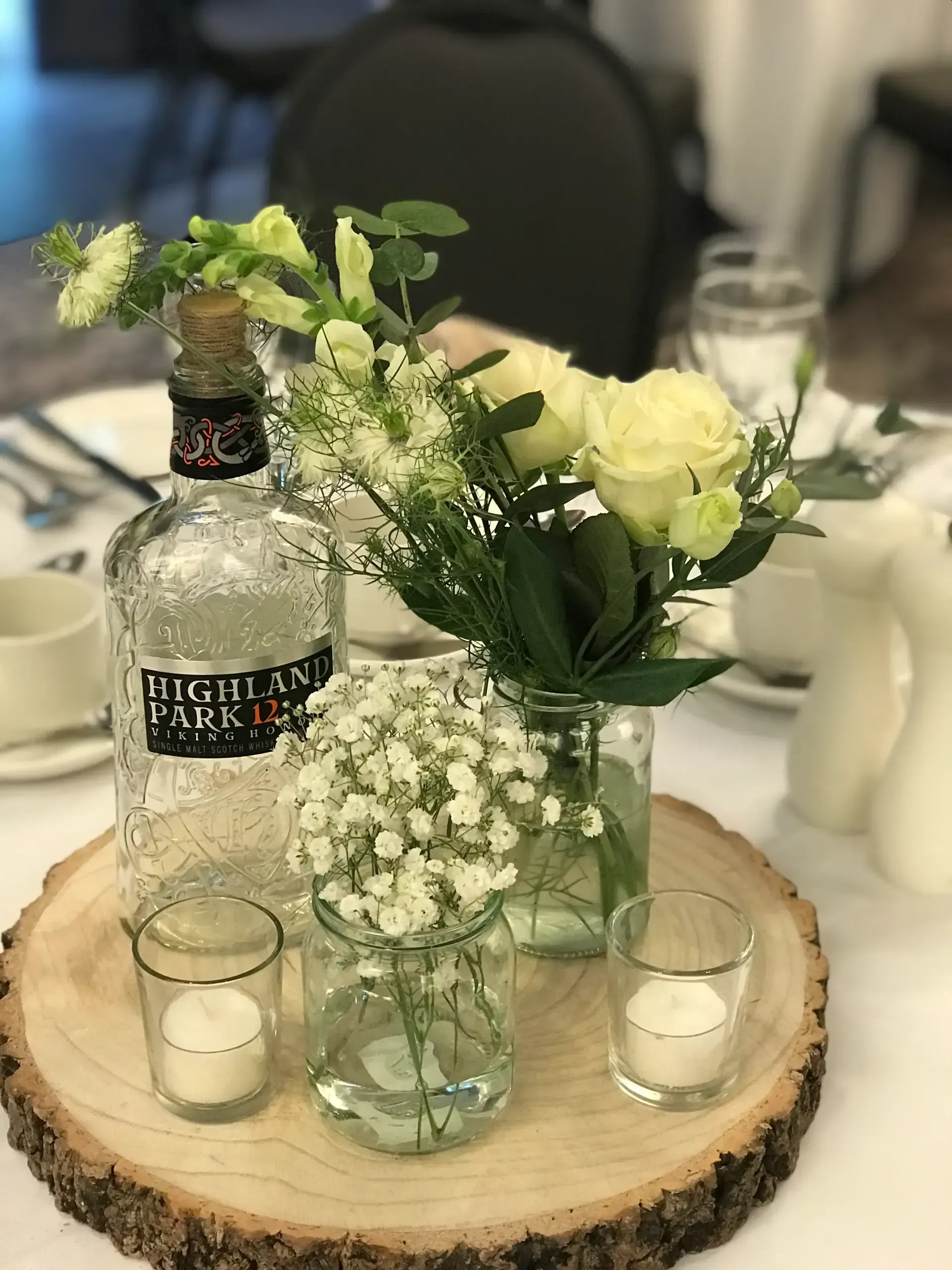 Flowers and a bottle centerpiece on a wood slab with candles at a table setting