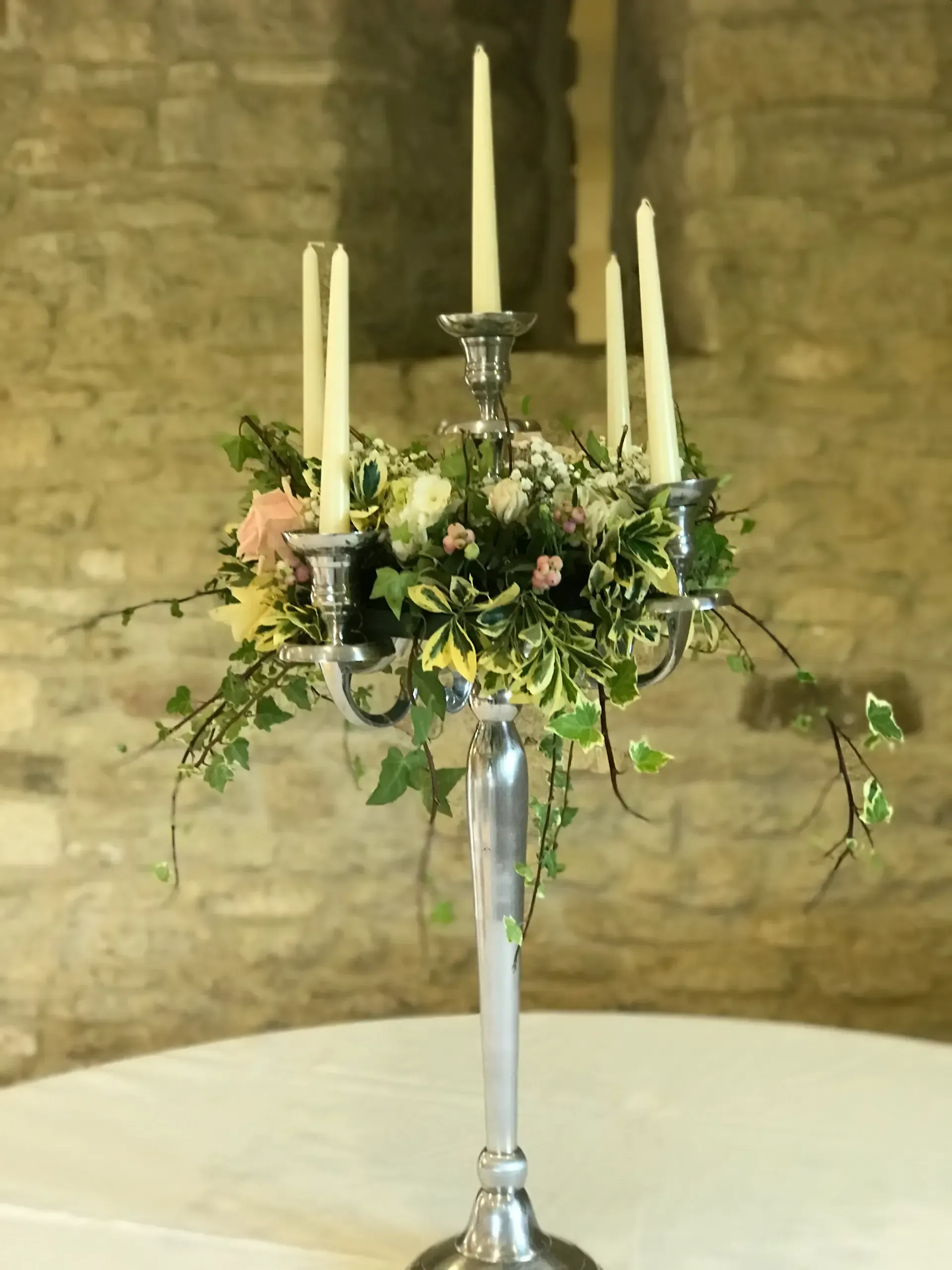 Floral candelabra centerpiece with white candles on a round table against a stone wall