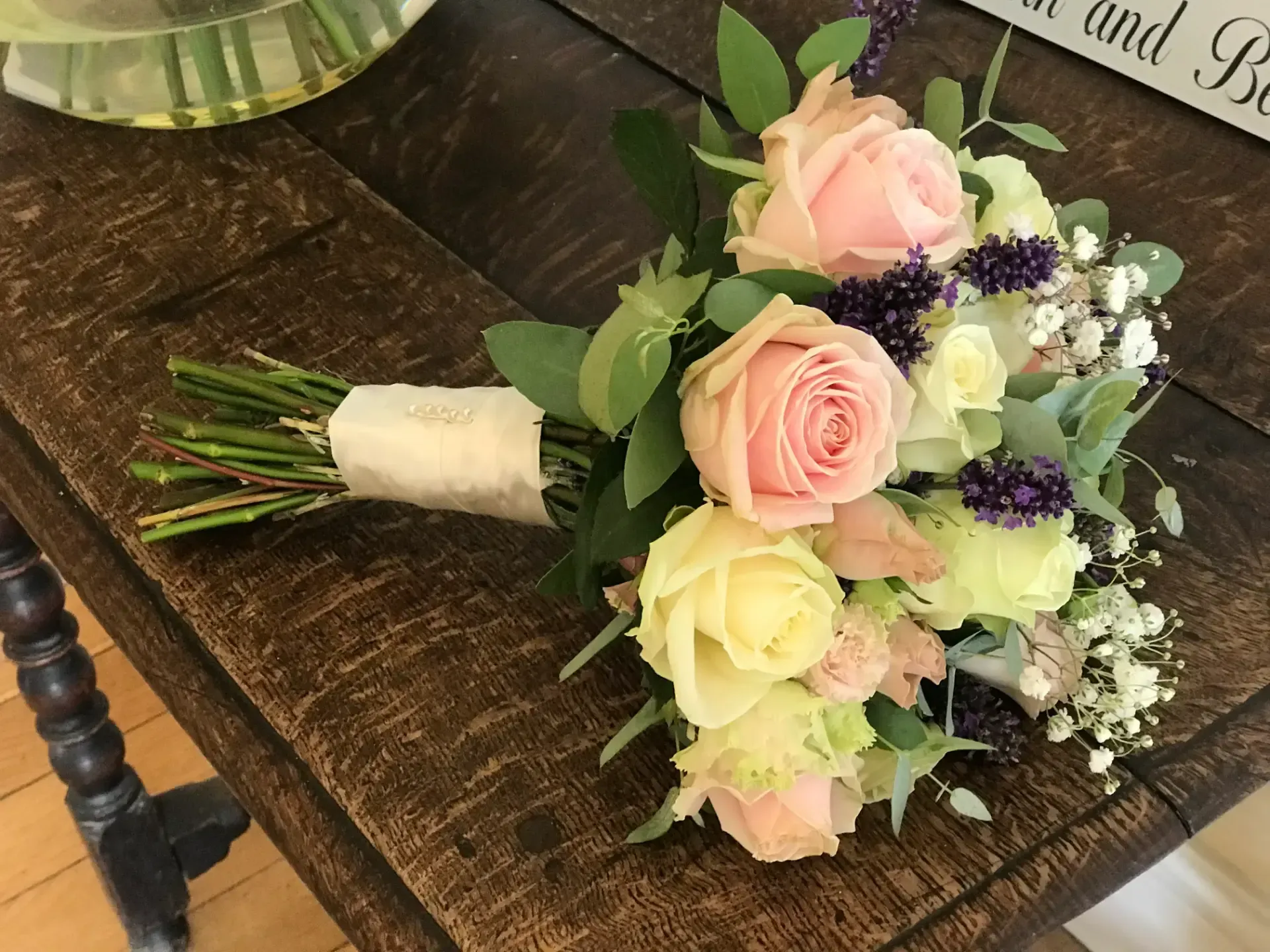 A pastel bouquet of roses and greenery on a dark wooden table