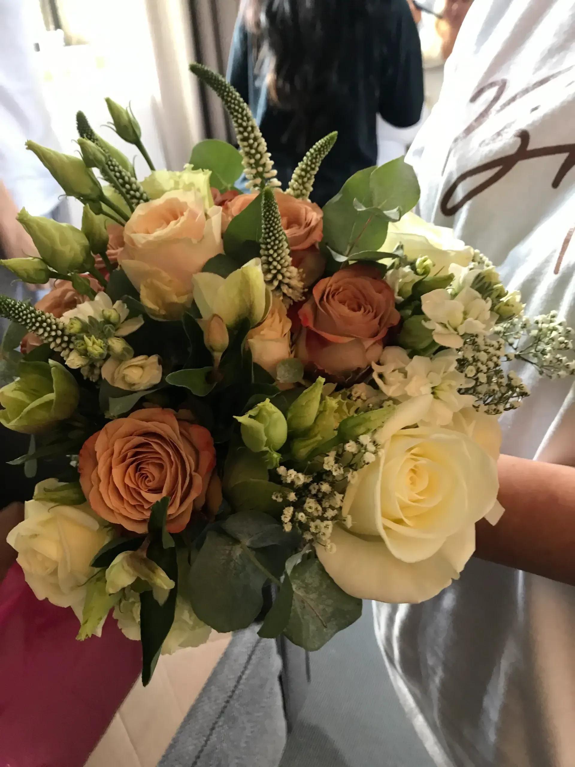 Bouquet of peach, cream, and white roses with greenery, held at an outdoor event