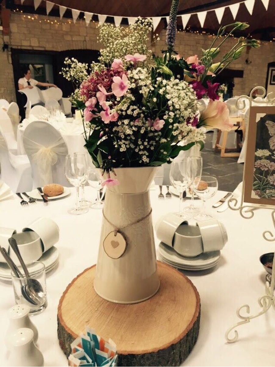 Floral centerpiece in a white vase on a wedding reception table with plates, glassware, and candles