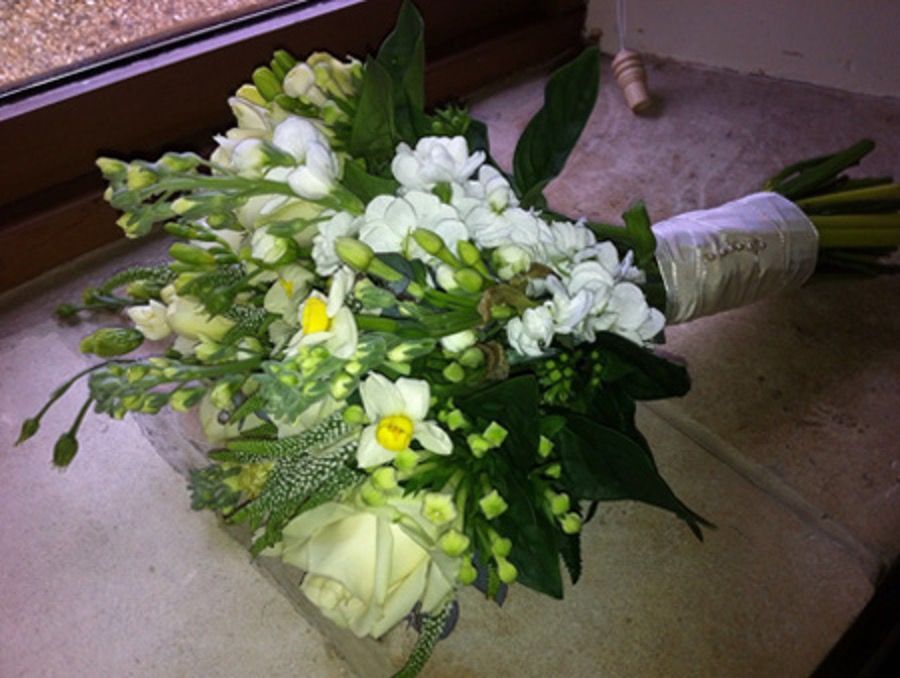White and yellow bridal bouquet resting on the floor with green foliage and wrapped handle