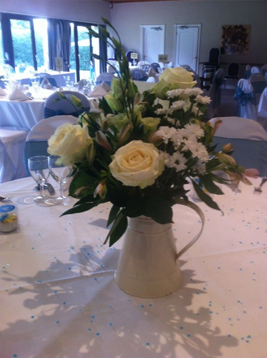 White rose centerpiece in a vase on a banquet table with tables and chairs in the background