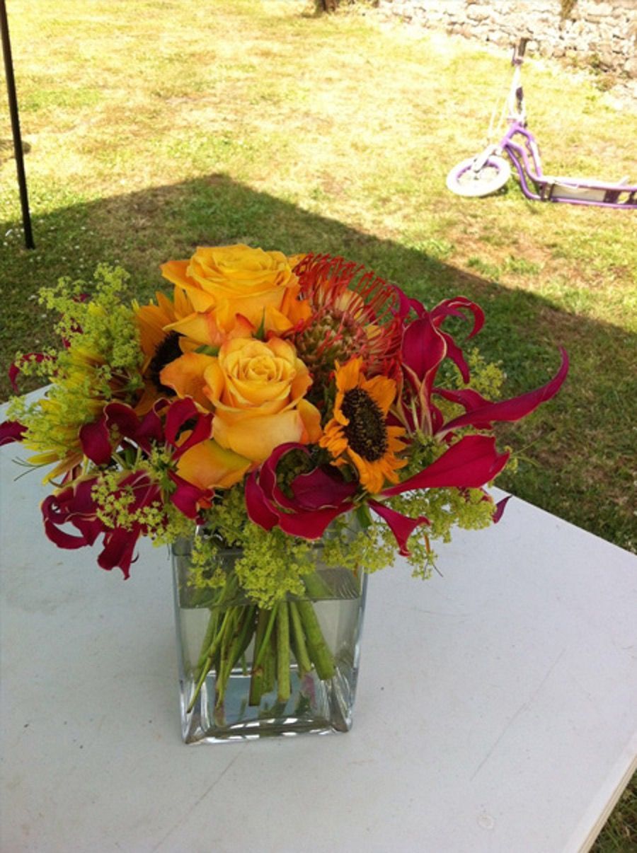 Bouquet of yellow and red flowers in a glass vase on a white table outdoors