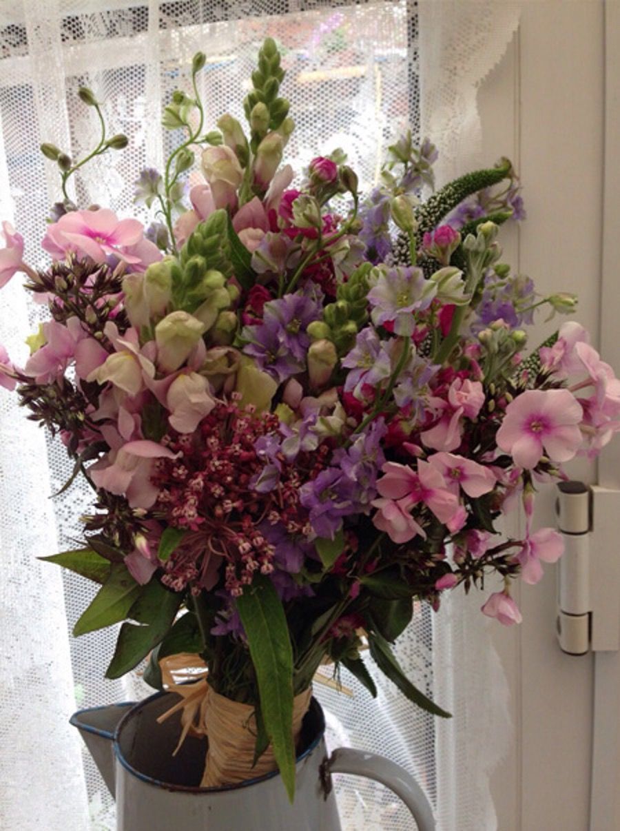Pink and purple mixed flower bouquet in a glass vase by a lace-curtained window