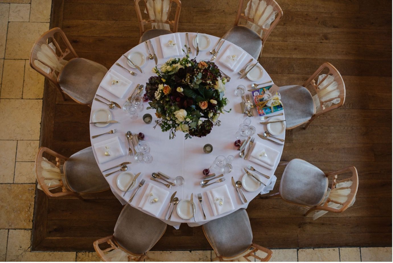 Overhead view of a round banquet table set with white linens, dishes, and a floral centerpiece on a wooden floor