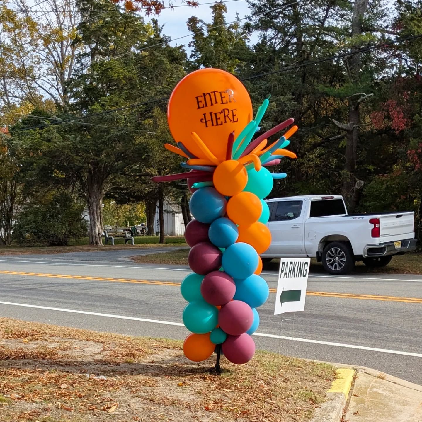 Colorful balloon column by roadside with orange “Enter Here” sign and white “Parking” sign