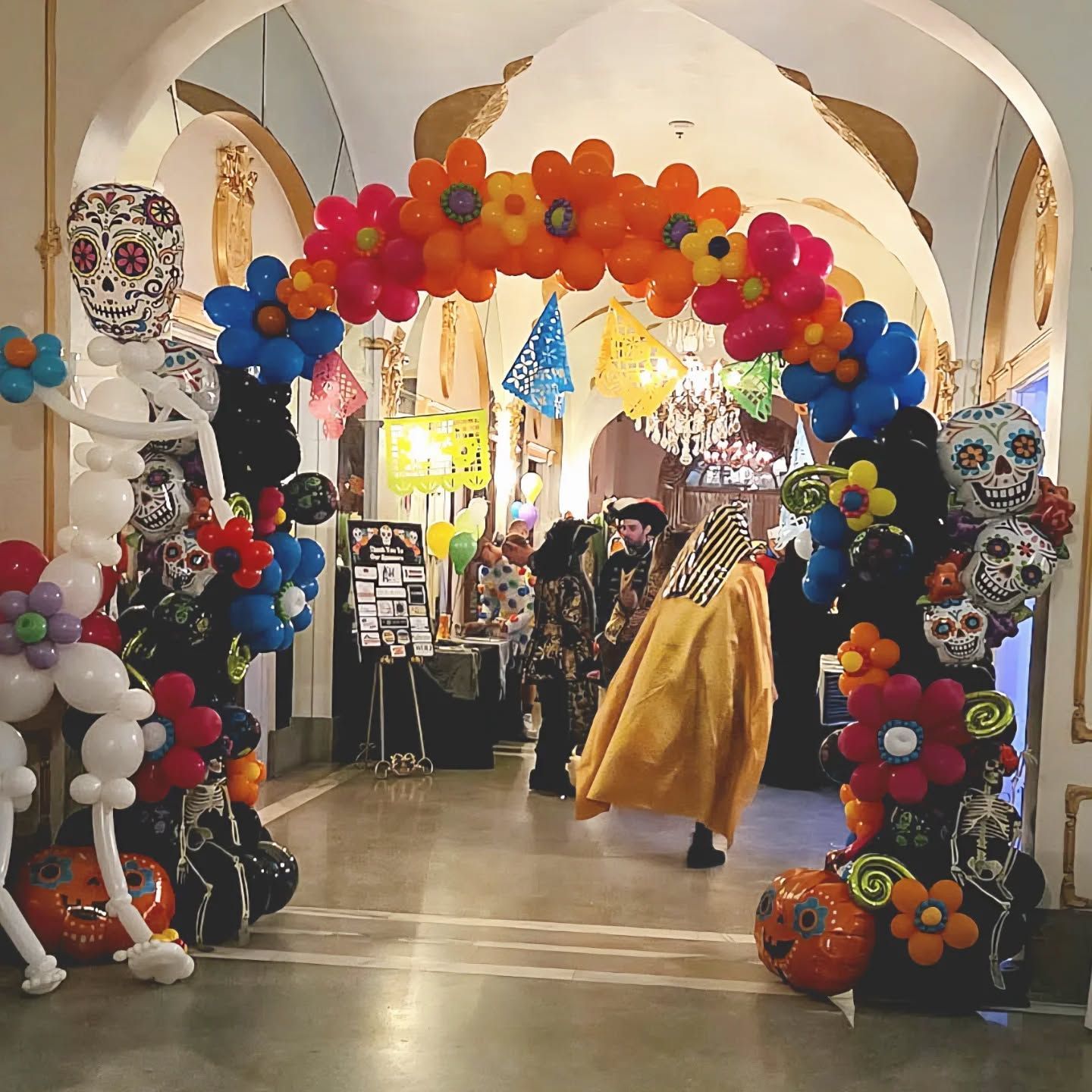 Decorated indoor corridor with colorful balloon arch and a person in a yellow costume walking through.