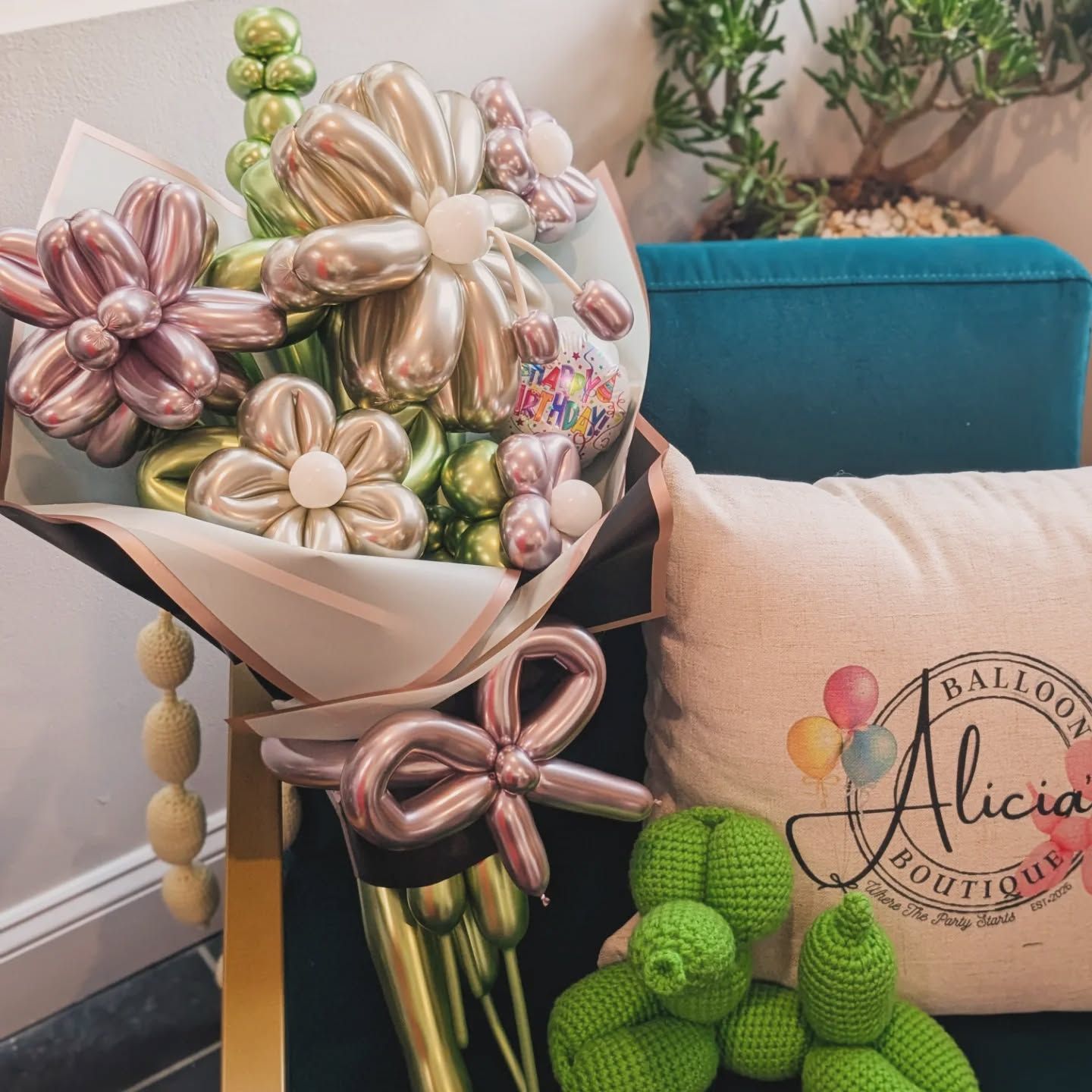 Balloon bouquet with pastel flower balloons beside a teal couch and a “Alicia” logo sign