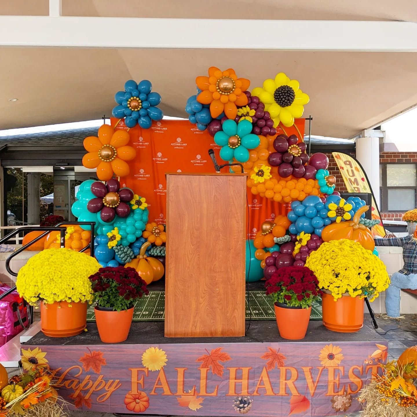 Colorful fall harvest display with pumpkins, flowers, and a wooden podium on a stage
