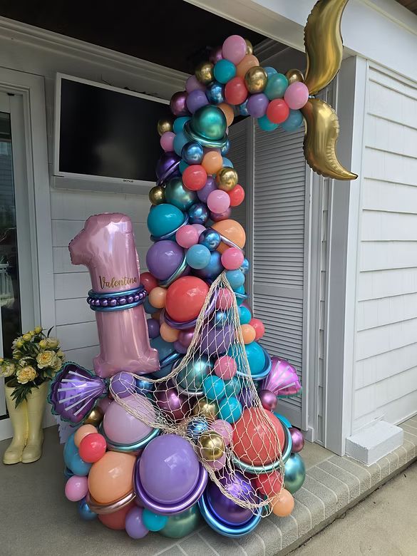 Colorful balloon sculpture of a pink high heel and gold number 1 on a porch with white siding