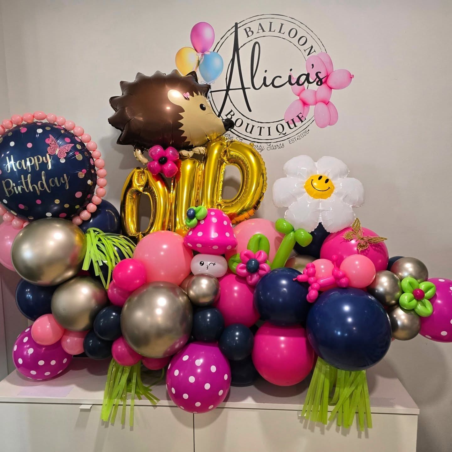 Birthday balloon display with pink, gold, navy, and silver balloons and a circular Alicia’s Balloon Boutique sign