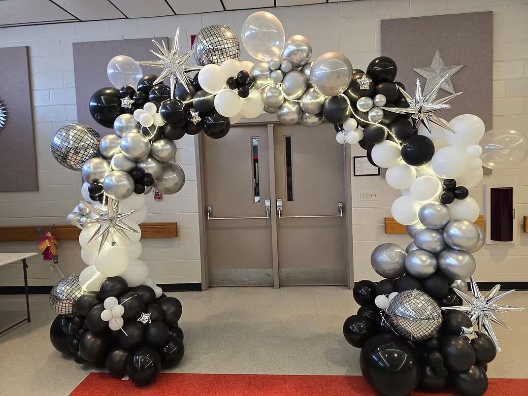 Black, silver, and white balloon arch framing double doors in a lobby