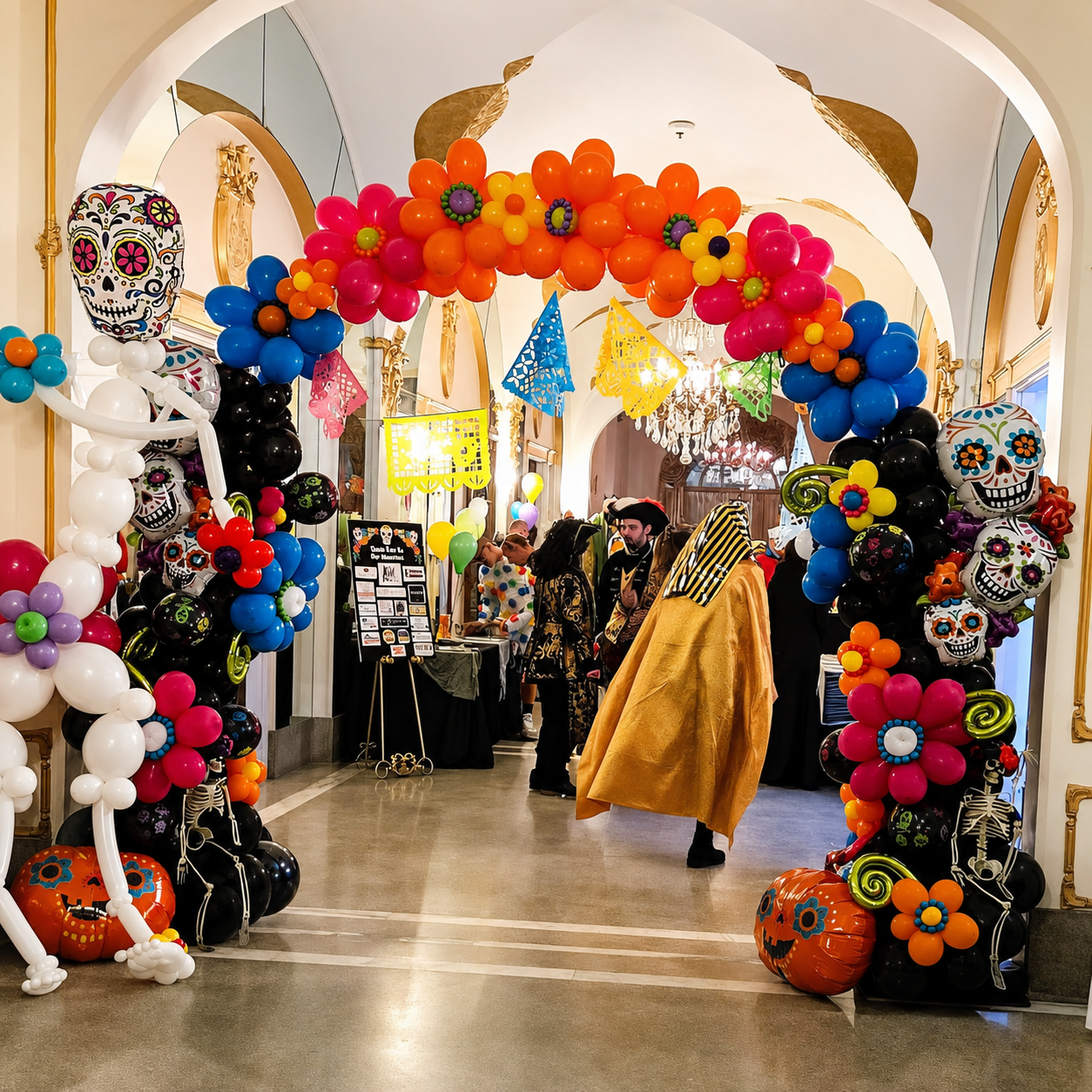 Colorful balloon arch frames a decorated indoor hallway with festive skull masks and Halloween décor.