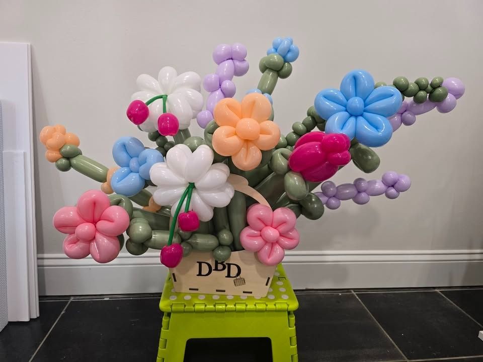 Colorful balloon flower arrangement in a vase on a lime-green crate against a white wall