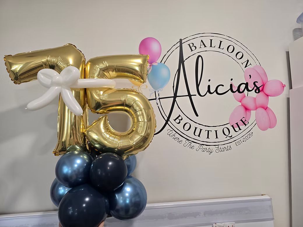 Gold balloon number 75 with blue balloon base beside a “Alicia’s” balloon-themed wall backdrop