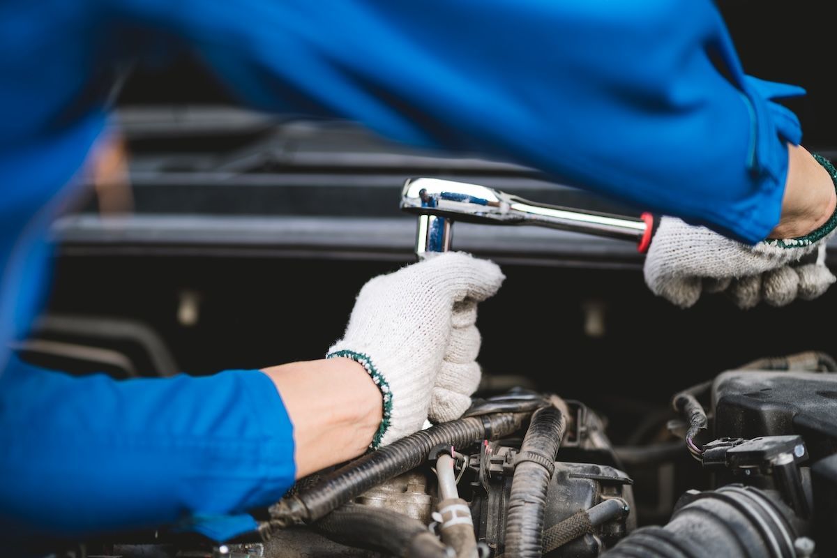 Mechanic in blue gloves using a ratchet to repair a car engine