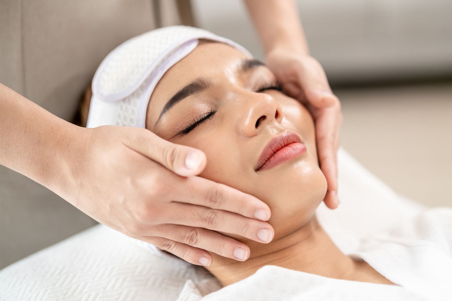 Facial massage in spa, with a client lying down and a therapist’s hands on her face
