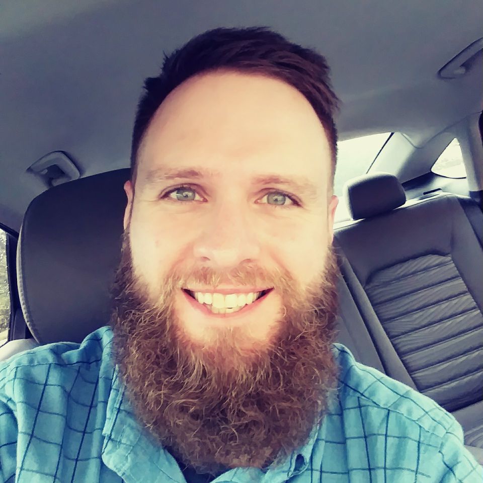 Smiling bearded man in a blue plaid shirt sitting in a car selfie