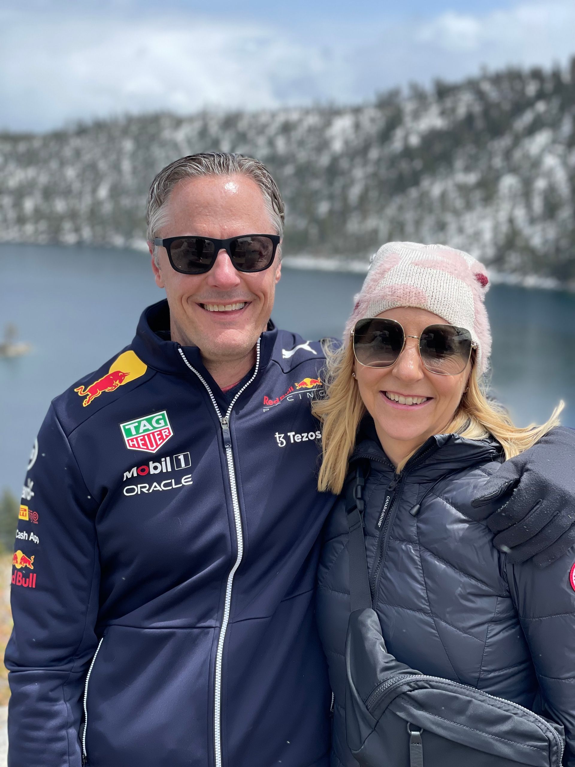 Two people in winter jackets and sunglasses smiling outdoors in a snowy mountain setting.