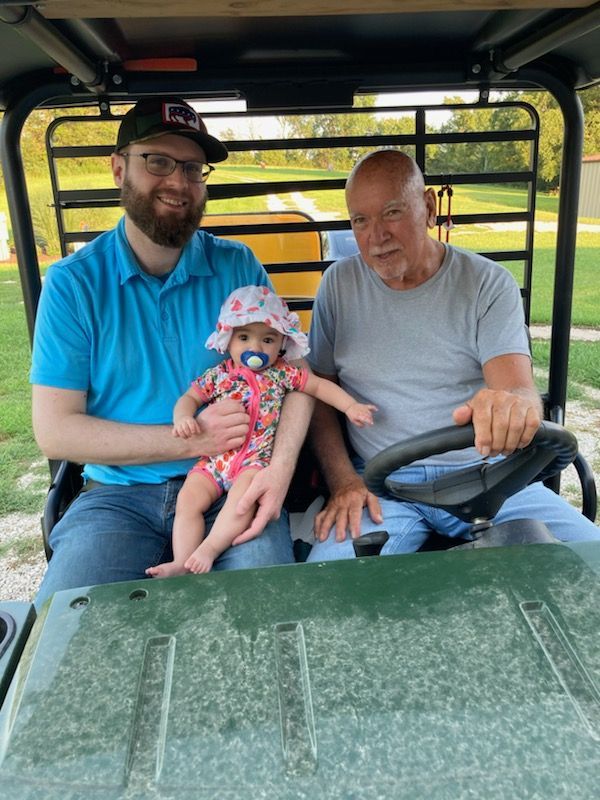 Three people sitting in a utility vehicle, smiling outdoors.