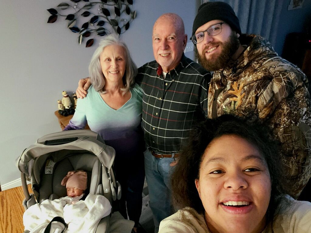 Family group posing indoors with a baby in a stroller and one person taking a selfie