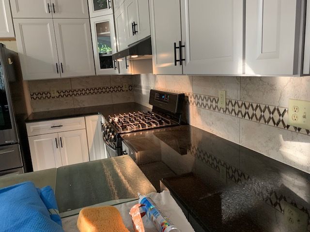 Kitchen with white cabinets, dark countertops, and tile backsplash featuring a decorative border.