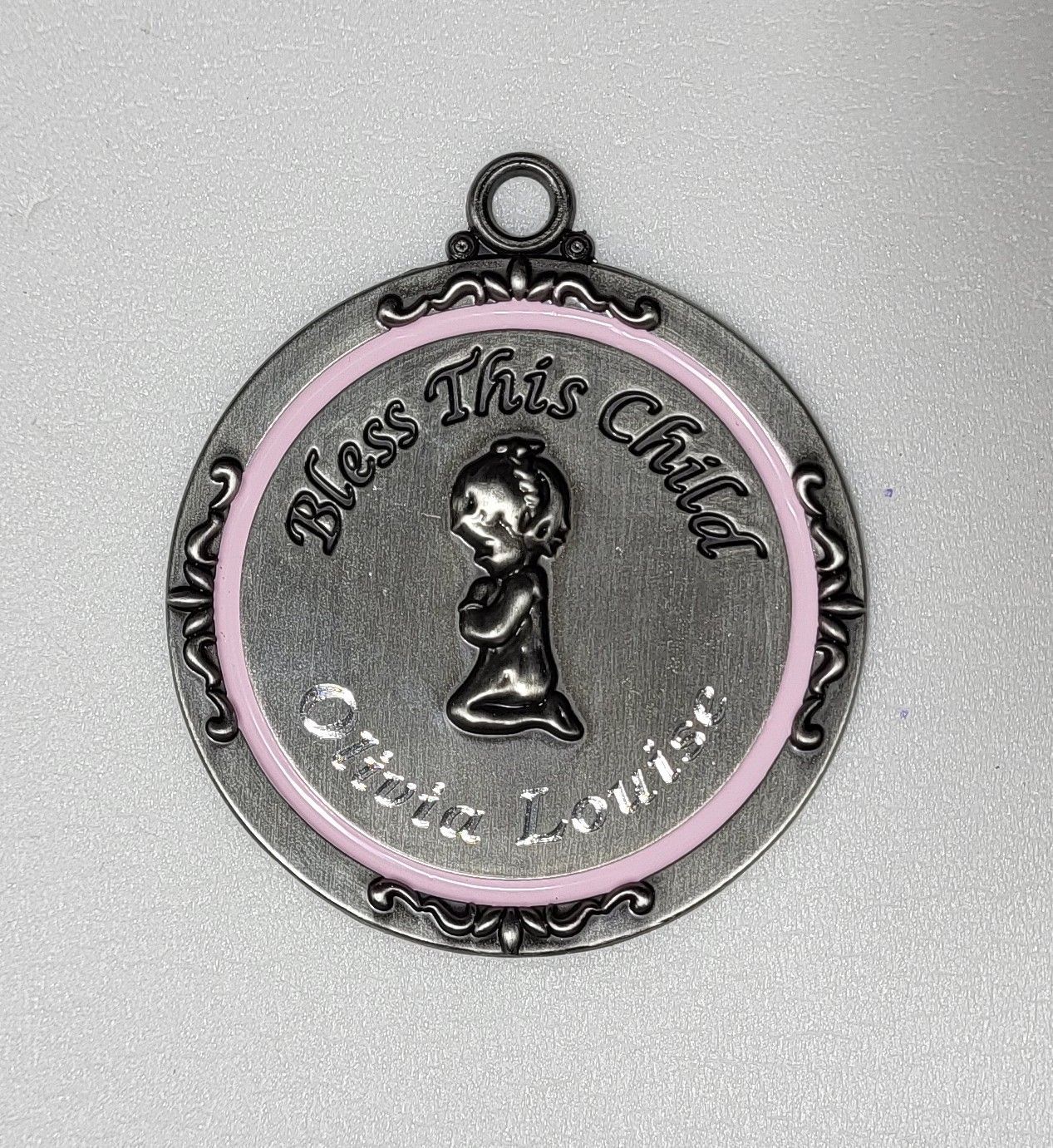 Round silver and pink “Bless This Child” pendant with a praying child figure center