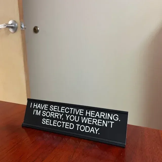 A black desk nameplate on a wooden surface reads, 
