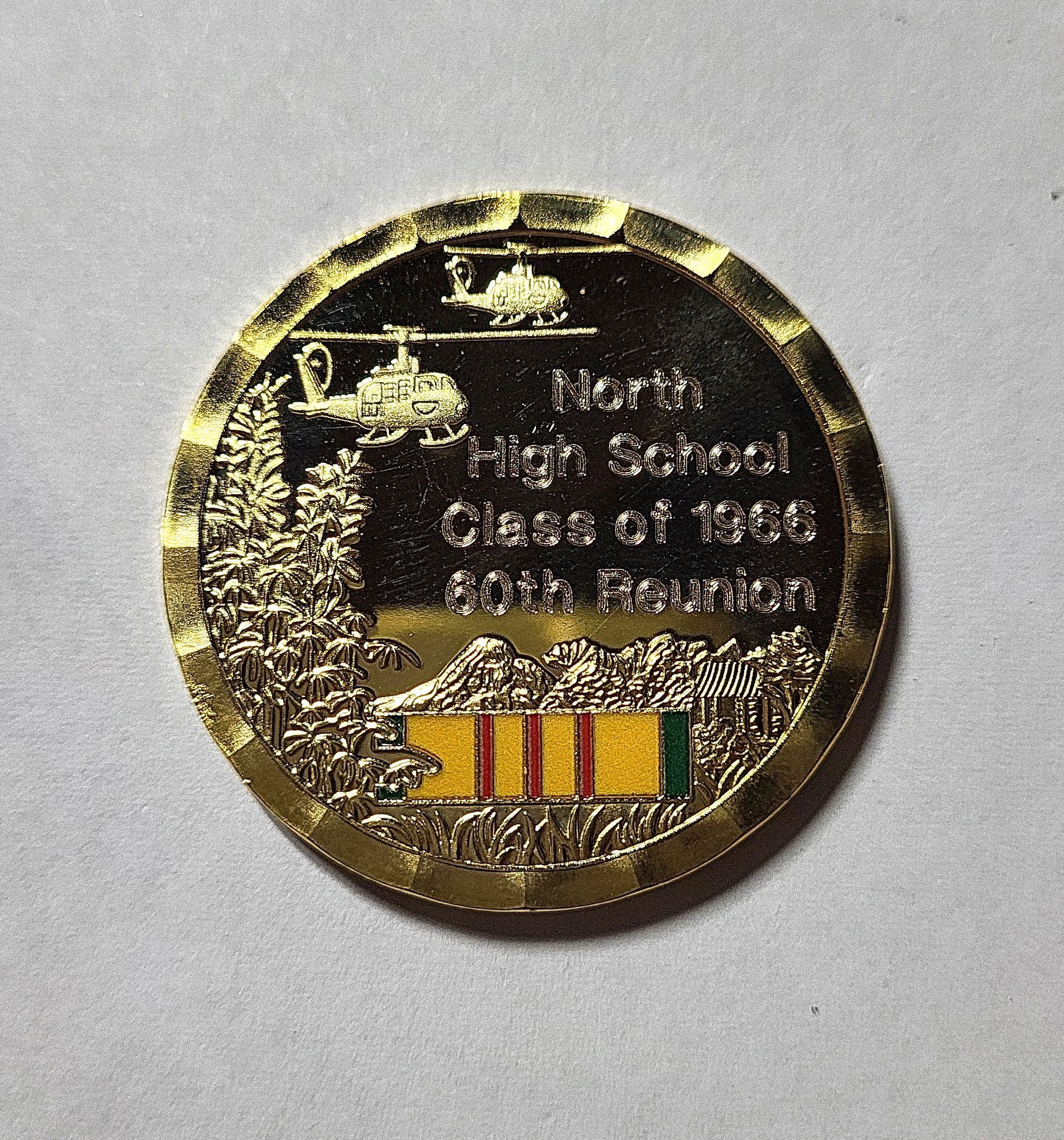 Round gold commemorative coin with etched text and a small multicolored striped emblem at the bottom.