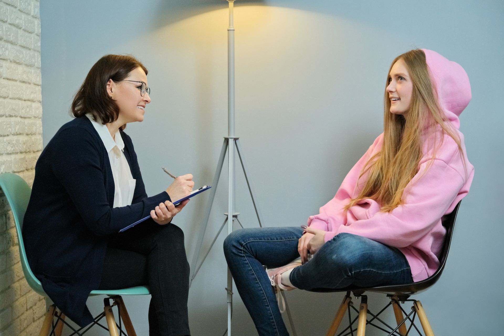 A woman is sitting in a chair talking to a young girl.