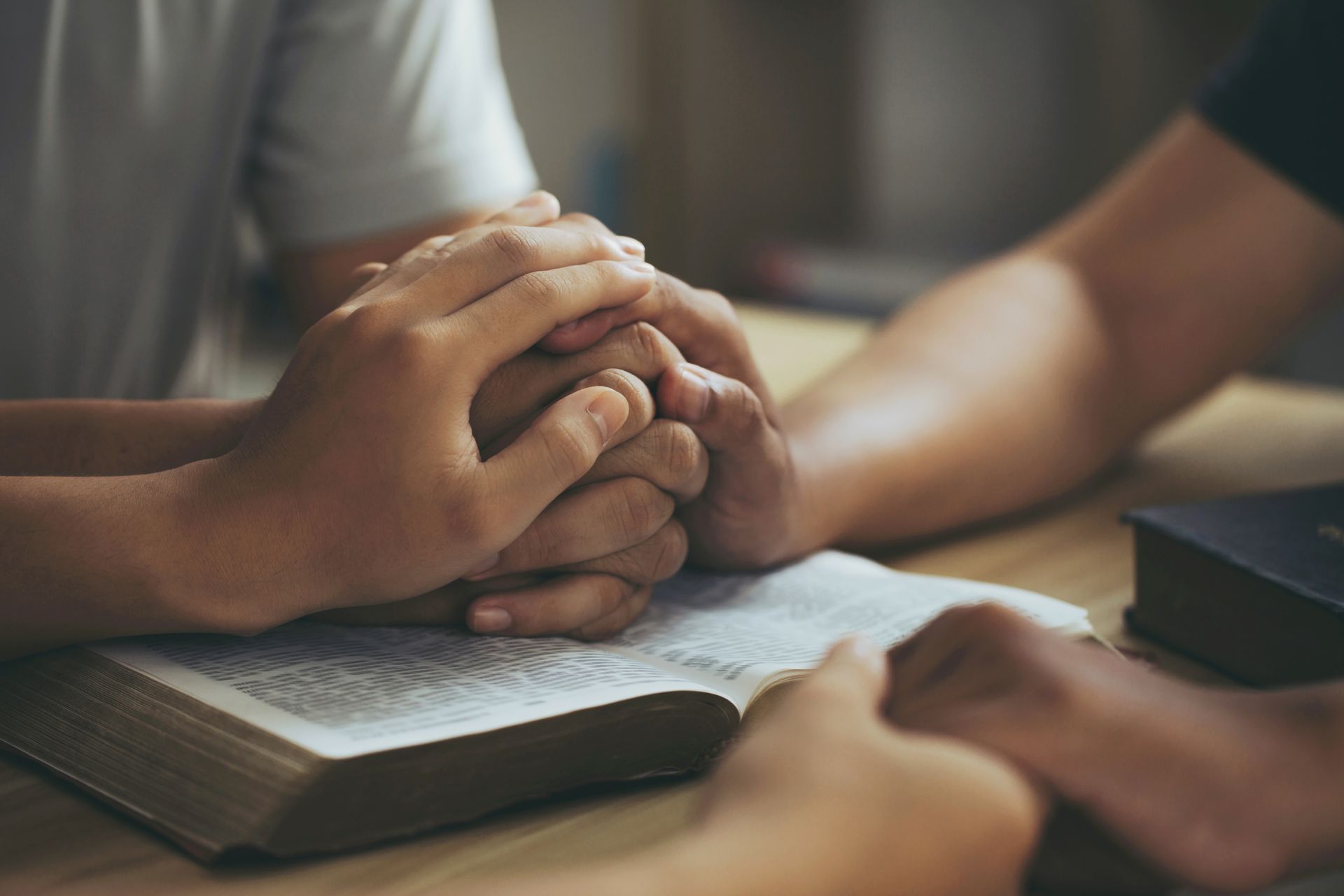 Two people are sitting at a table with their hands folded over a bible.