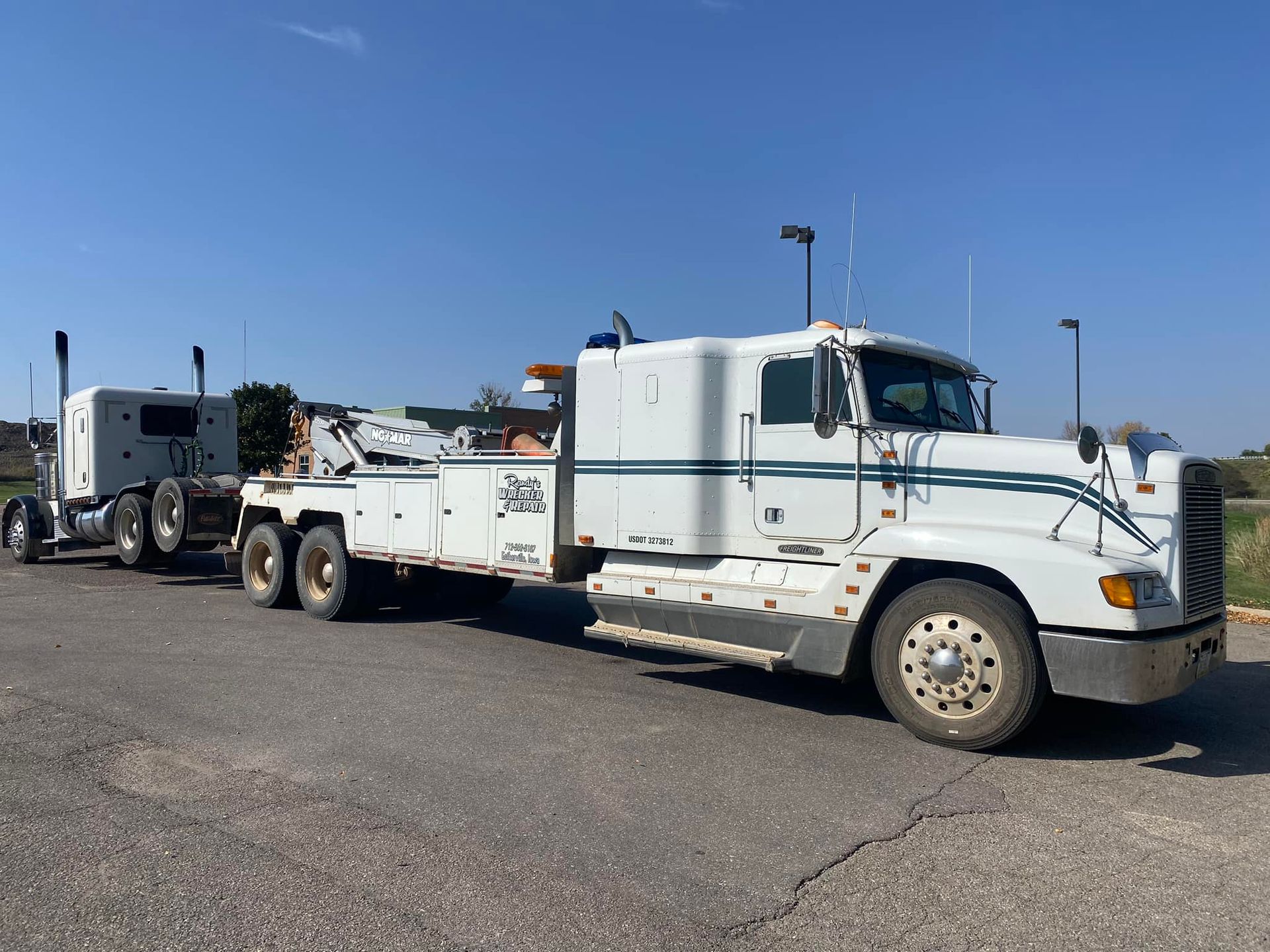 White tow truck hauling a semi-truck on asphalt on a sunny day.