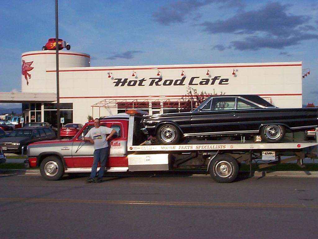 A tow truck with a car on the back is parked in front of a hot rod cafe