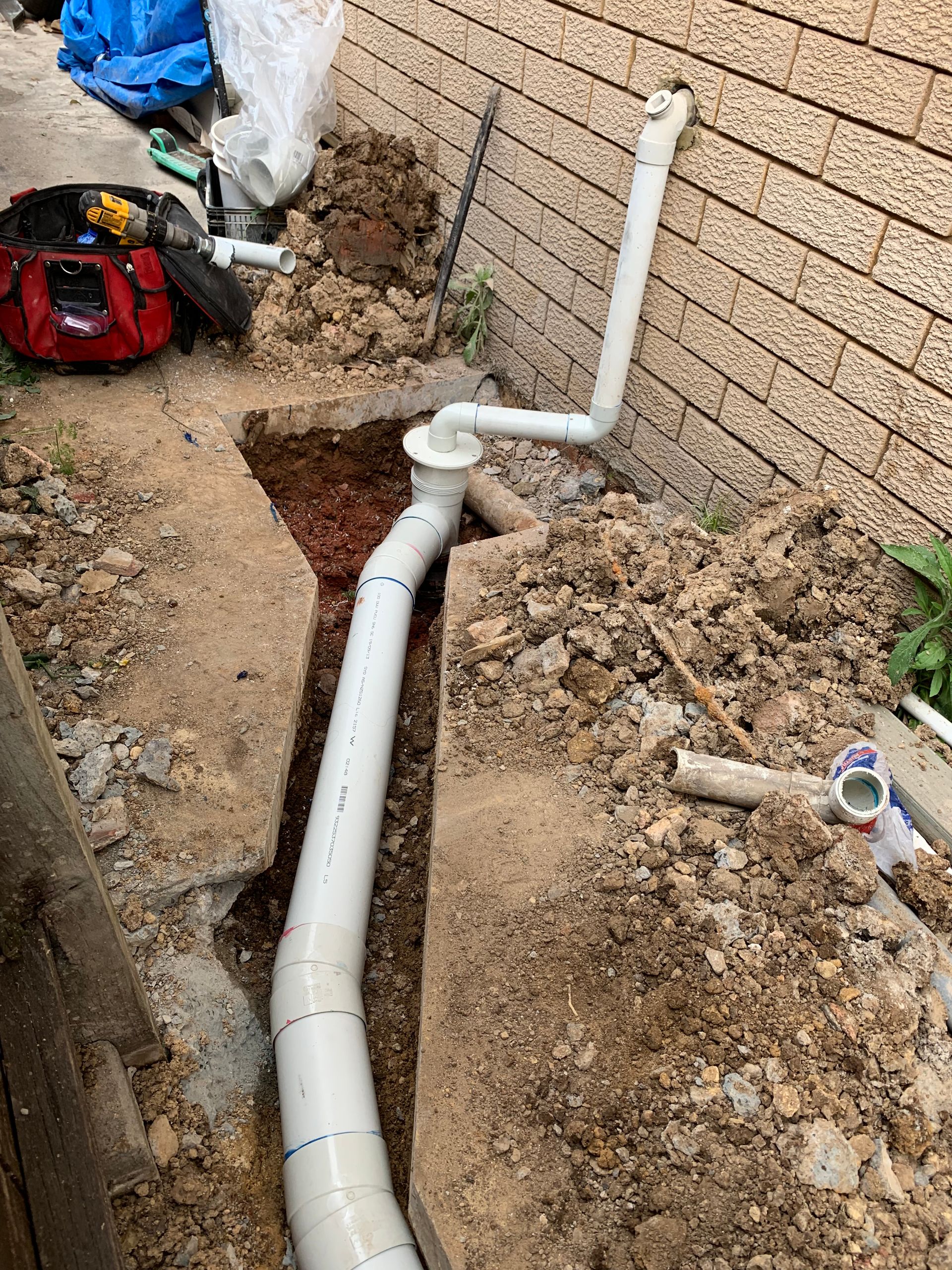 Trench Dug With White PVC Pipes Being Installed Near a Brick Wall — Start 2 Finish Plumbing in Caringbah, NSW