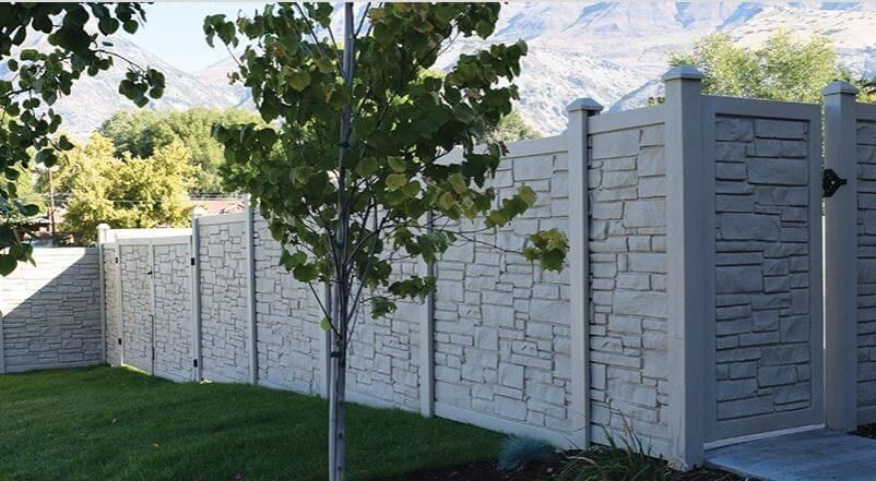 White stone privacy wall with metal gate beside a small tree and grassy yard, mountains in the background