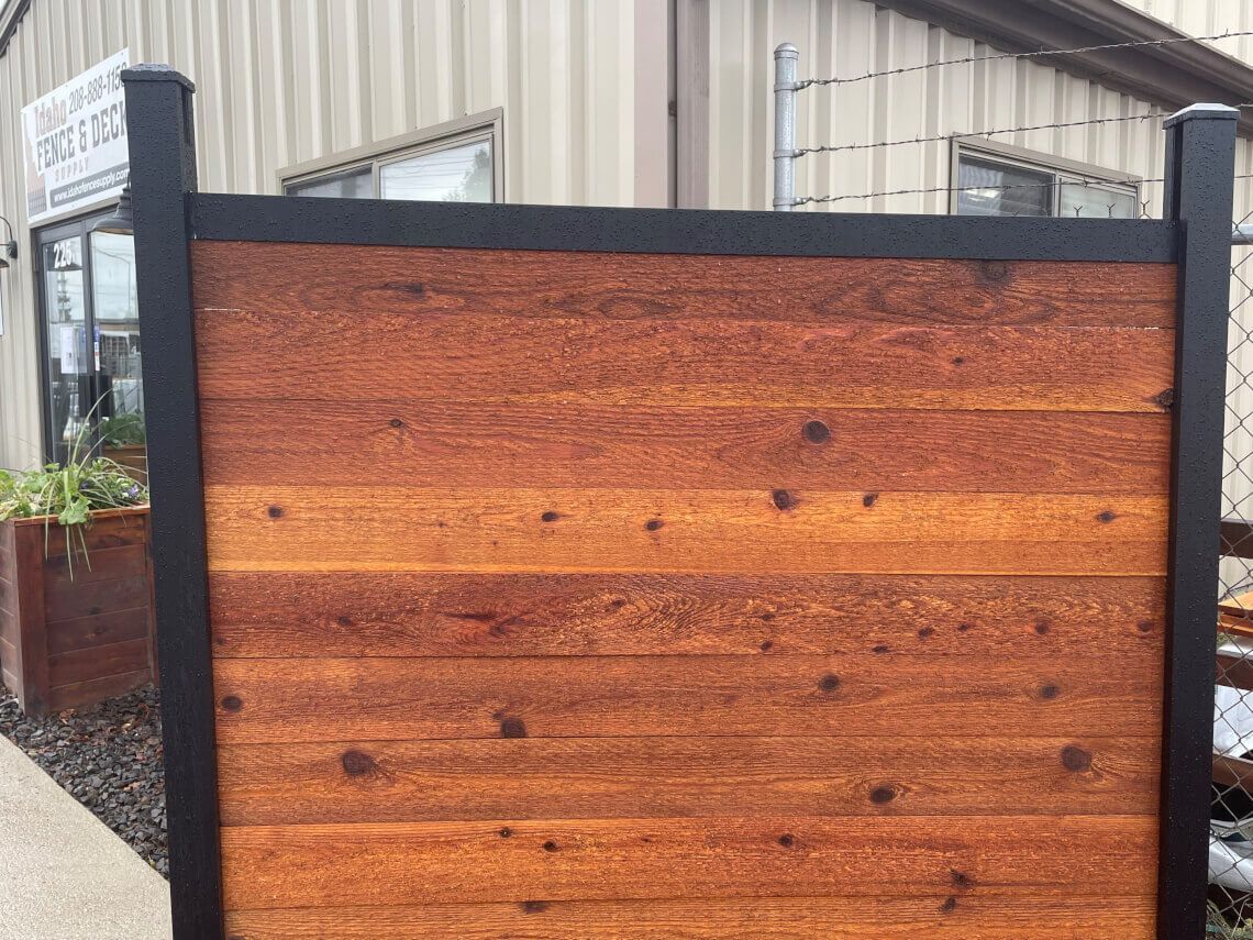 Wooden privacy fence with black posts in front of an industrial building