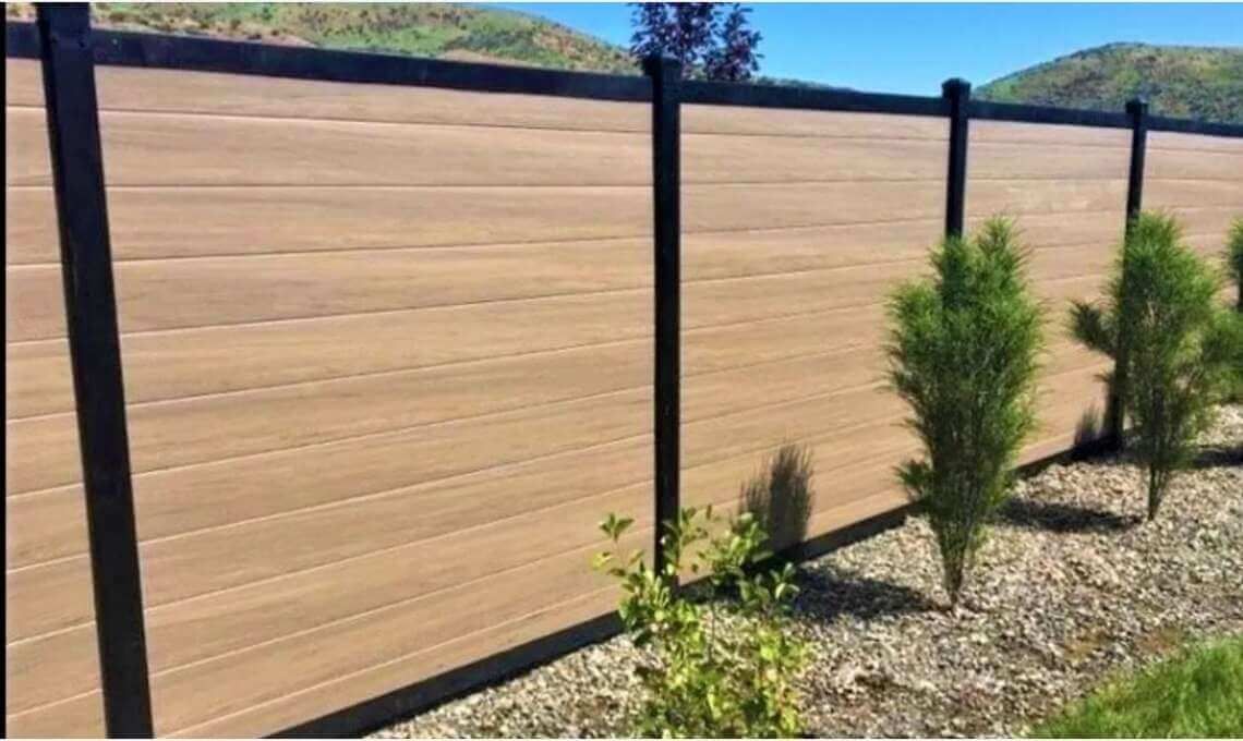 Wooden privacy fence with black posts along a gravel yard, with small green shrubs in front