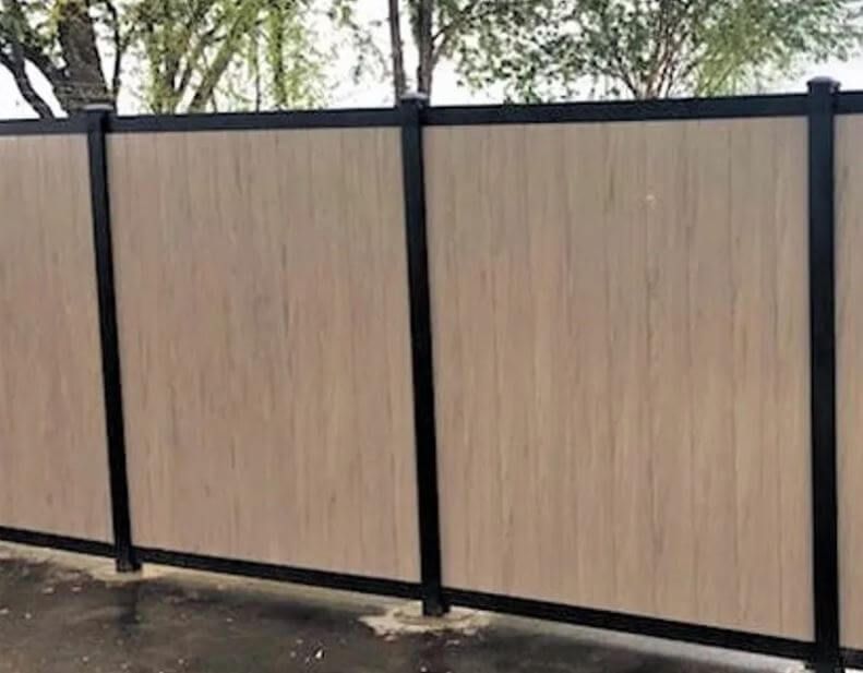 Tall beige privacy fence with black metal posts along a dirt path outdoors