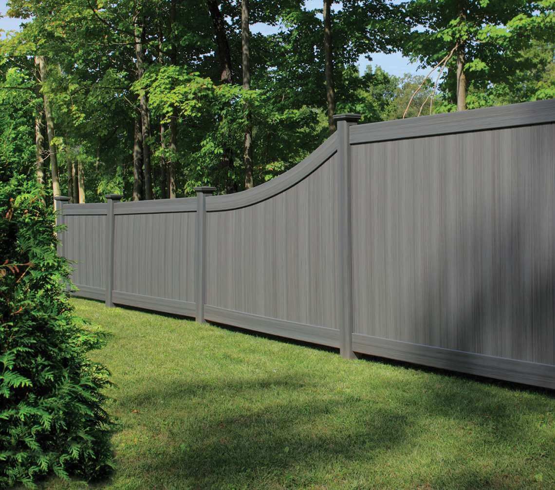 Gray vinyl privacy fence along a grassy yard with trees in the background