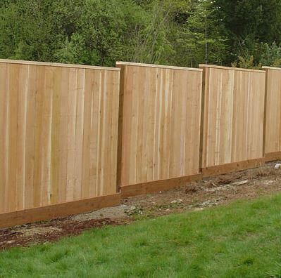 New wooden privacy fence along a grassy yard, with trees in the background