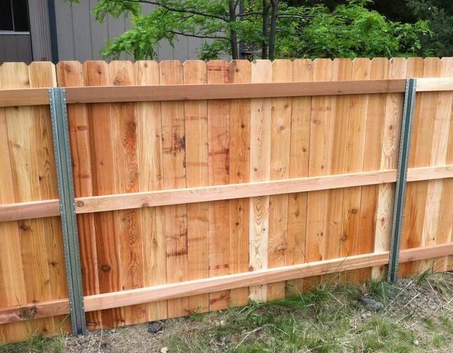 Wooden backyard fence with a blue vertical support post and grass along the bottom