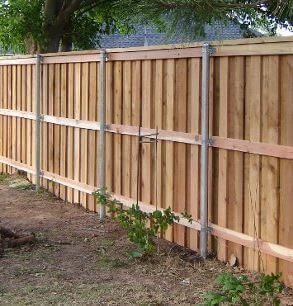 Wooden privacy fence with a gate along a yard, made of vertical tan planks and horizontal supports.