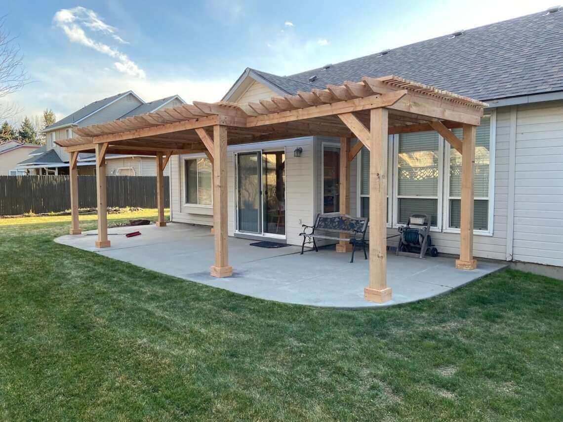 Backyard patio with a wooden pergola, concrete slab, and sliding glass doors on a house