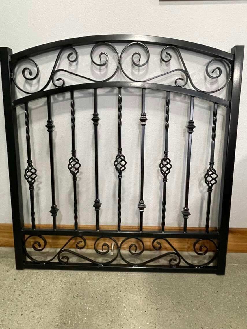Decorative black wrought-iron fireplace screen with scrollwork and vertical bars against a light wall