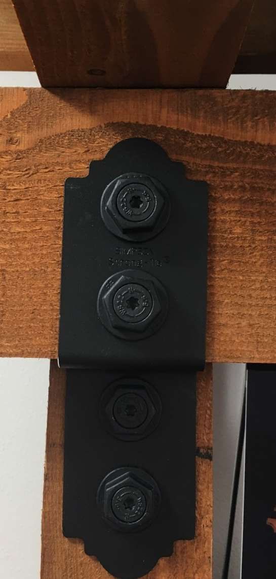 Black metal bracket with four circular fasteners mounted on a wooden beam