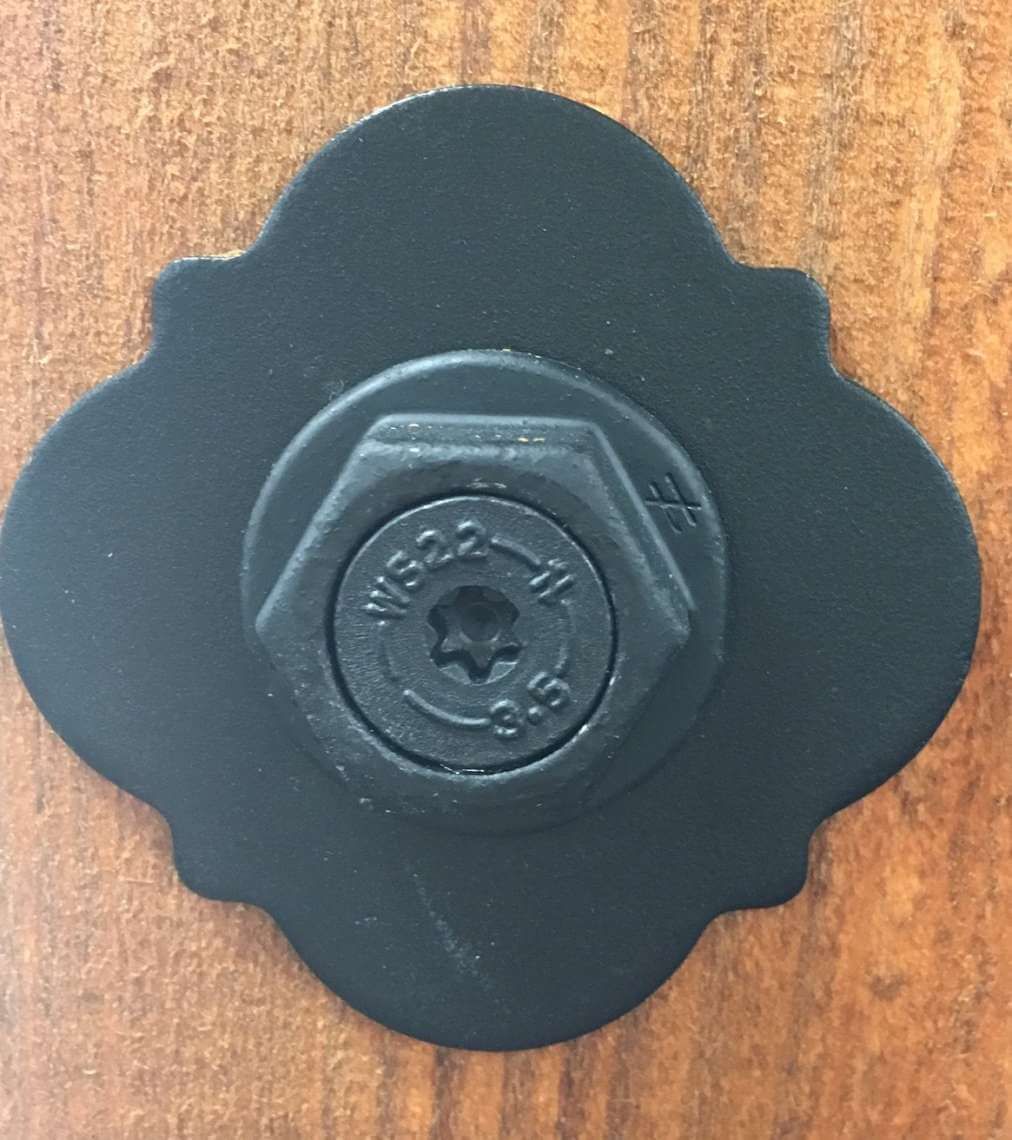 Black flower-shaped metal knob with a central bolt on a wooden surface