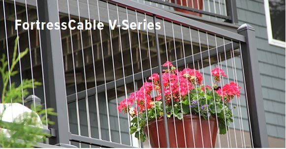 Red flower planter hanging from a balcony with metal cable railing in front of a house