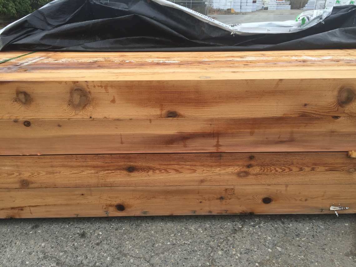 Stacked wooden planter box with weathered planks and black plastic lining on pavement.
